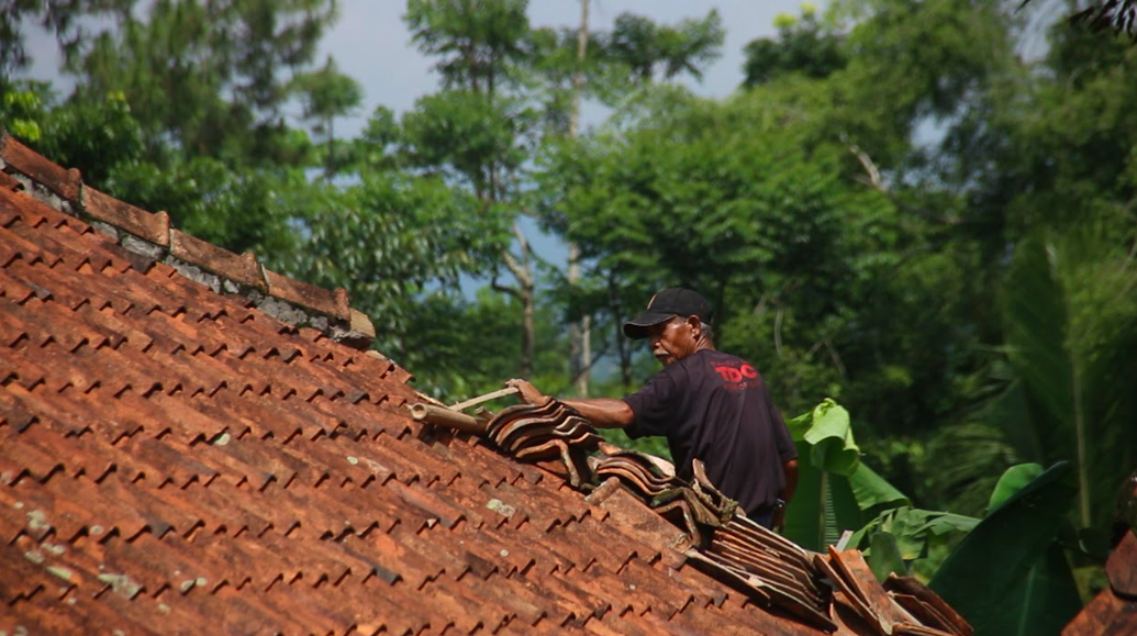 Seorang warga menaiki atap rumah yang rusak akibat getaran gempa