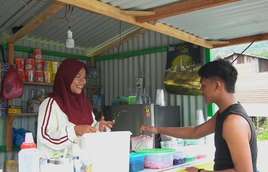 Warga Desa Babah Suak, Firna (22), tersenyum saat melayani pembeli di kios kecil miliknya di Kecamatan Beutong Ateuh Banggalang, Kabupaten Nagan Raya, pada Rabu (7/10/2026). Foto: (Mardili/Bithe.co). Salinan ini telah tayang di https://www.bithe.co/news/suara-air-yang-dirindukan-petani-beutong-ateuh/index.html#google_vignette.
